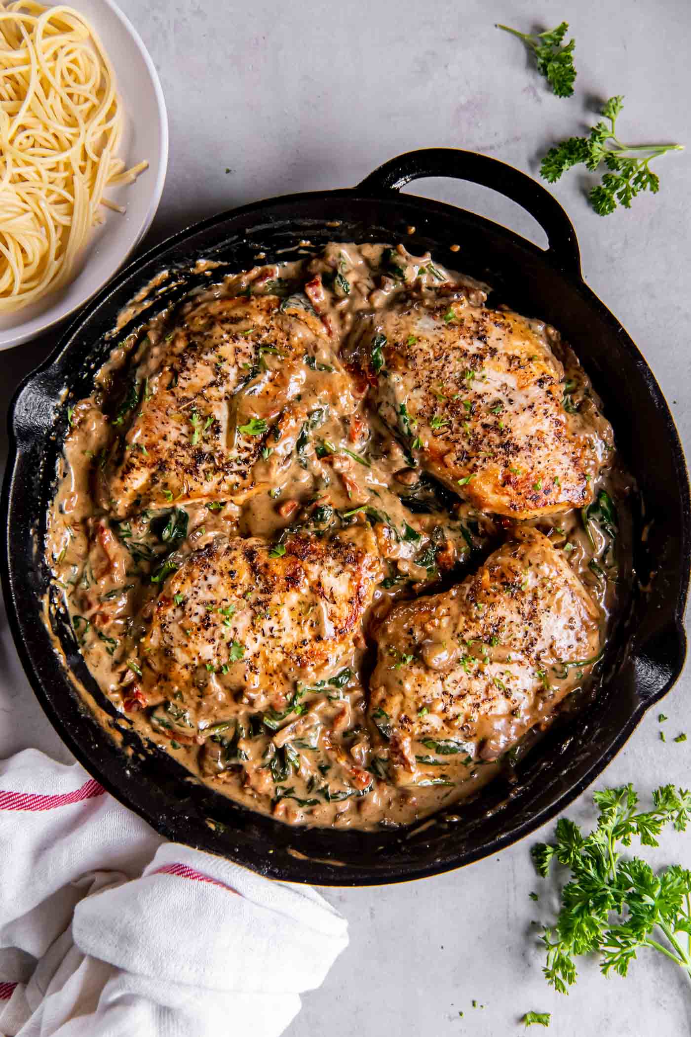 Four chicken breasts with creamy Tuscan sauce in a cast iron skillet.