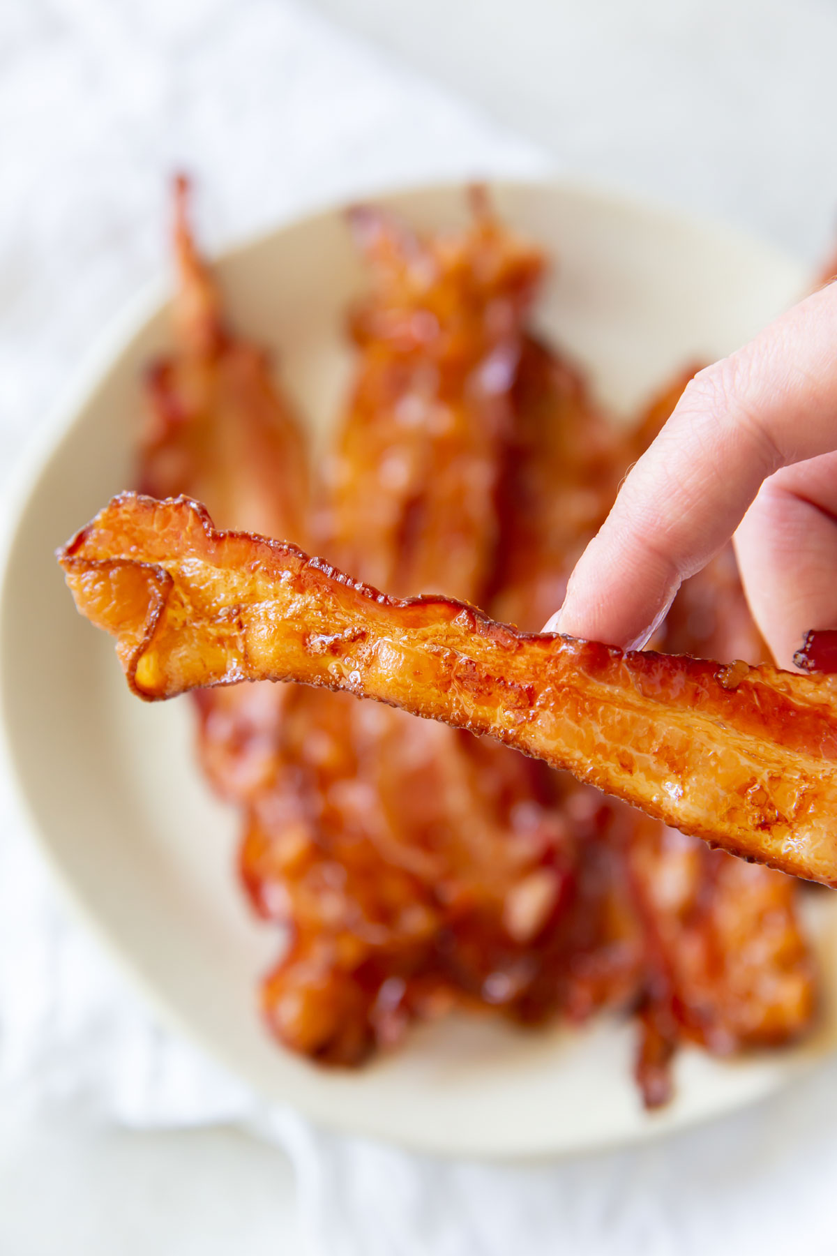 hand holding a slice of bacon over a plate of bacon