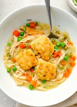 Serving of crockpot chicken and dumplings in a white bowl with a spoon.