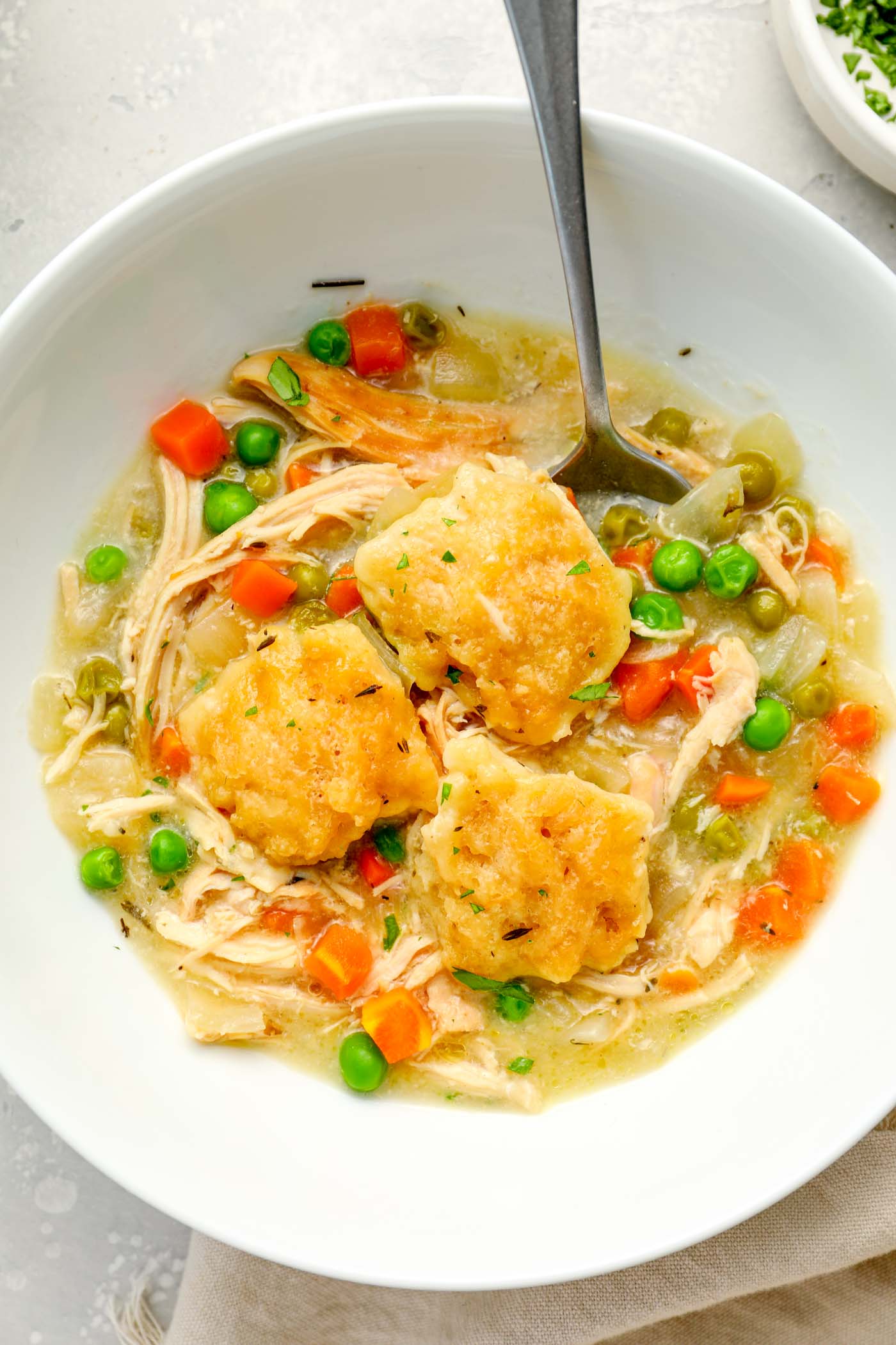 Serving of crockpot chicken and dumplings in a white bowl with a spoon.