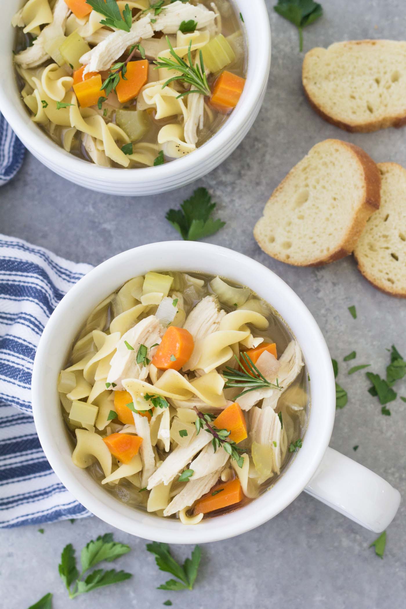 Crock pot chicken noodle soup served in two soup bowls with sliced bread on the side.