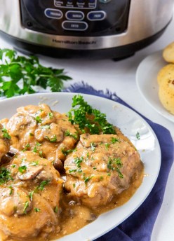 Pork chops smothered with gravy on a plate with slow cooker in background.