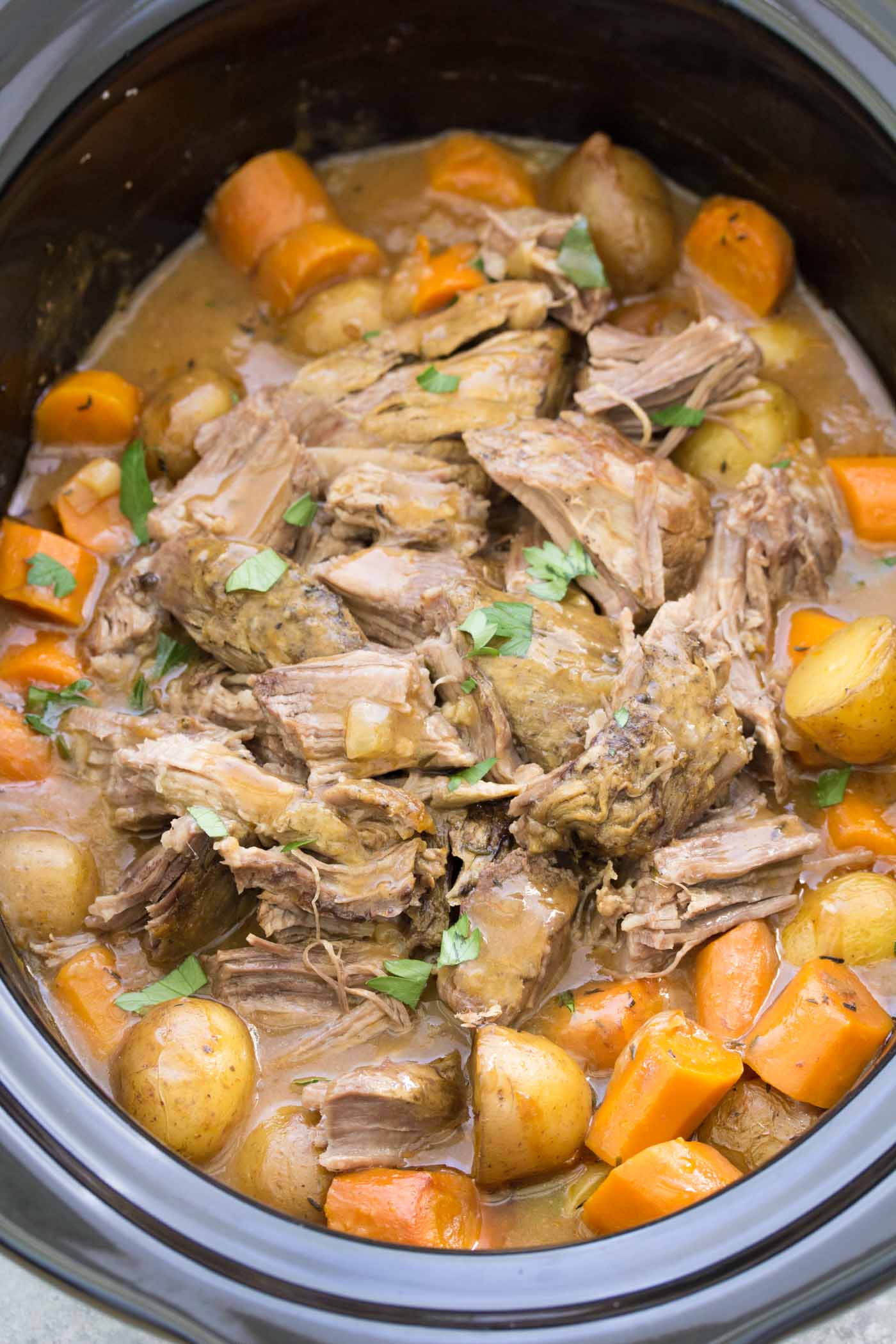 Crock pot roast shredded in a slow cooker, with potatoes, carrots and gravy.