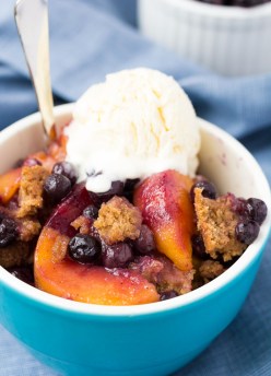 Crockpot peach cobbler with blueberries, topped with vanilla ice cream.