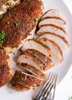 Sliced crockpot chicken breast on plate with whole chicken breasts.