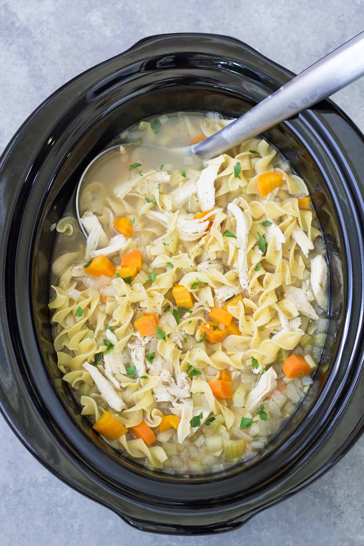 Crockpot chicken noodle soup in a slow cooker with a ladle.