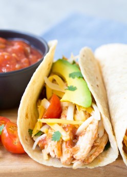 Close up side view of crockpot chicken tacos with salsa, avocado and tomatoes.