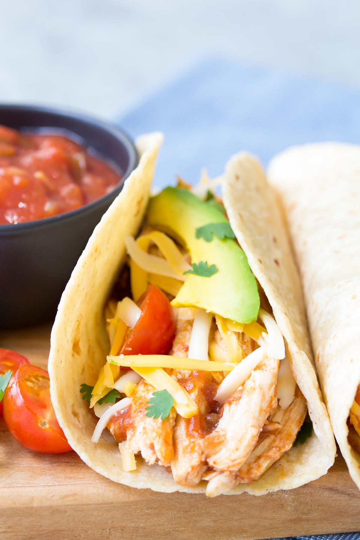 Close up side view of crockpot chicken tacos with salsa, avocado and tomatoes.