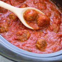 Meatballs and sauce in crockpot with wooden spoon.