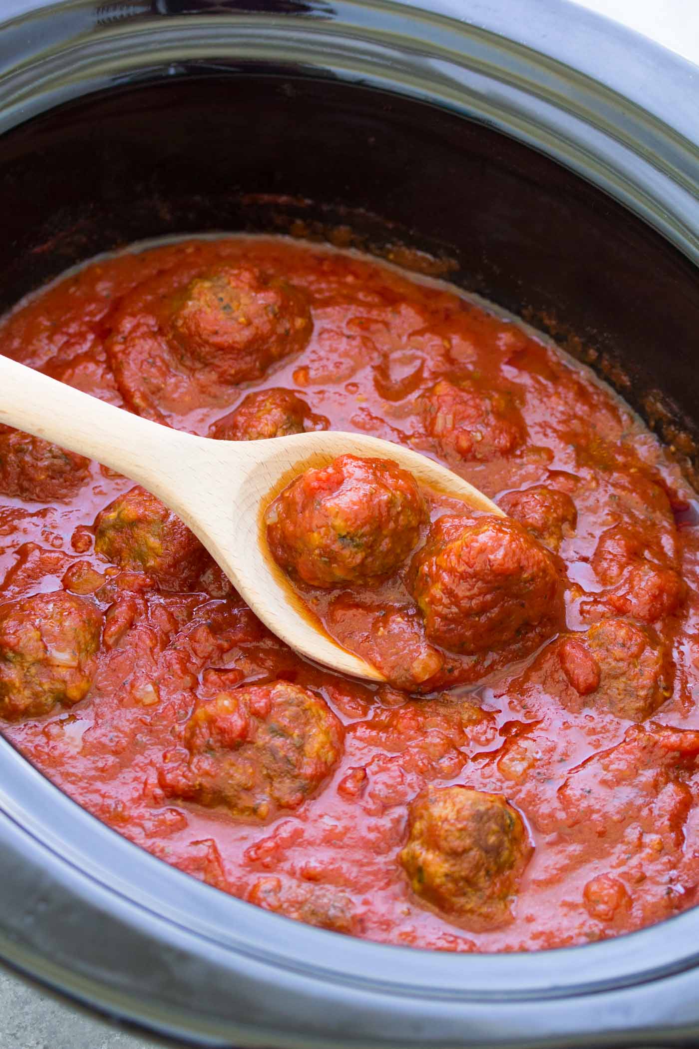 Italian meatballs and marinara sauce in slow cooker with wooden spoon.
