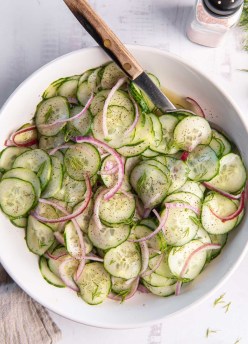 Cucumber salad in a white serving bowl with a serving spoon.