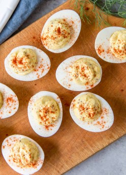 Deviled eggs with paprika on a wood serving board.