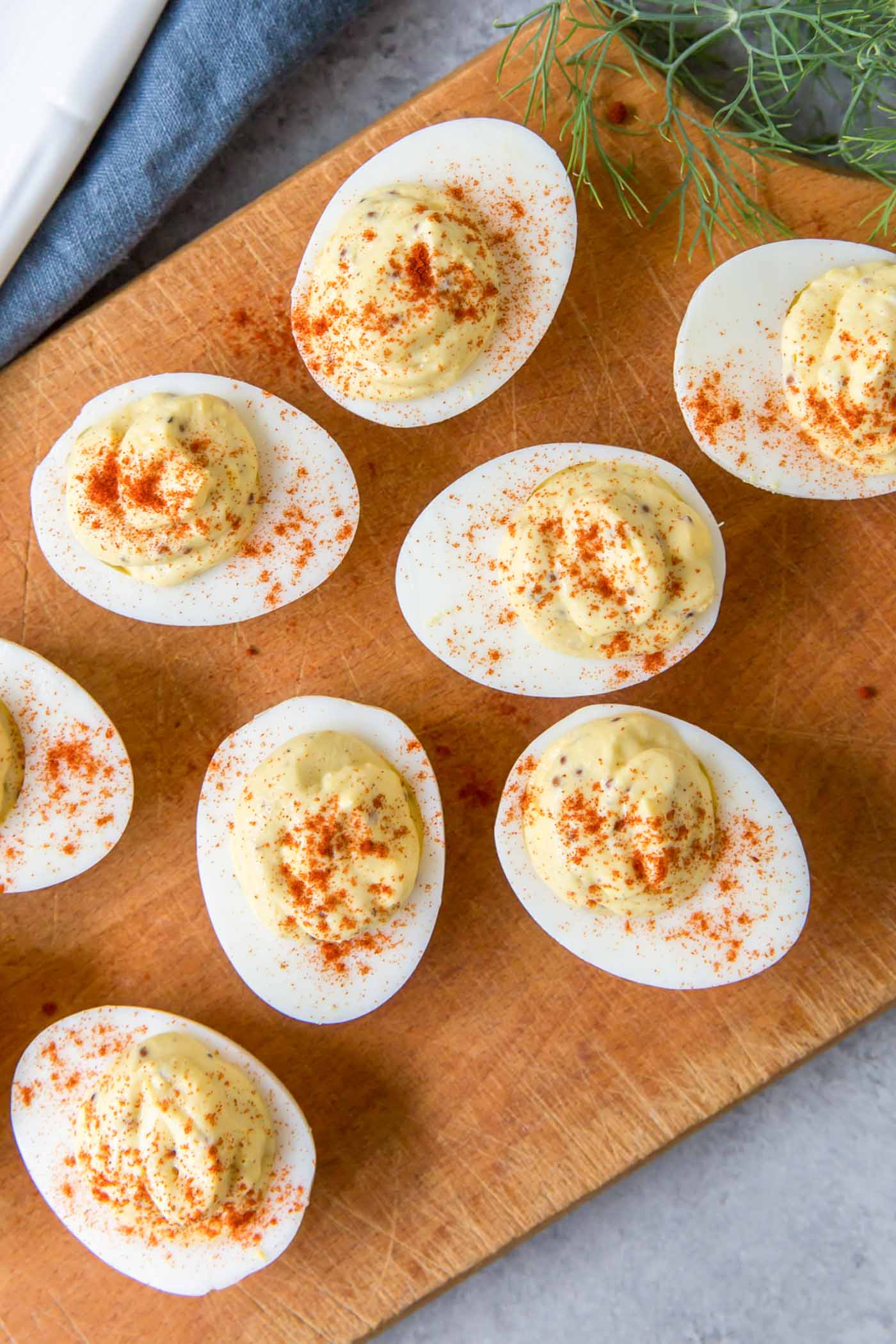 Deviled eggs with paprika on a wood serving board.
