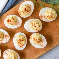 Deviled eggs with paprika on a wooden serving board.