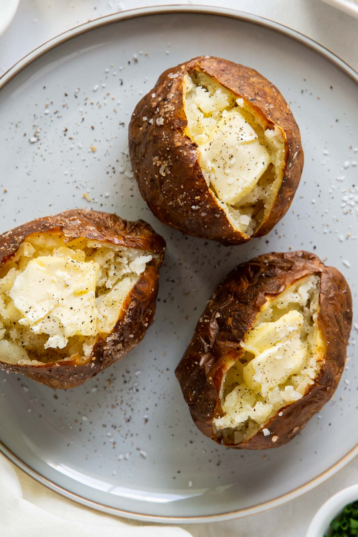 Three baked potatoes topped with butter, salt and pepper on a plate.