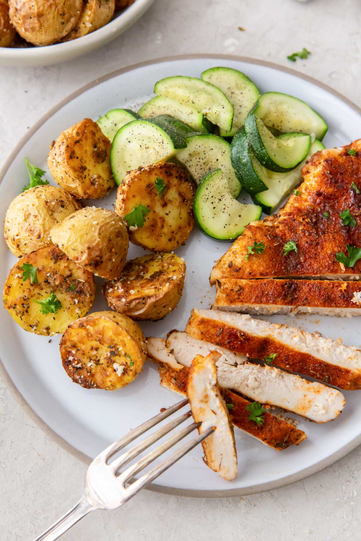 Air fryer chicken breast served with air fryer potatoes and zucchini.
