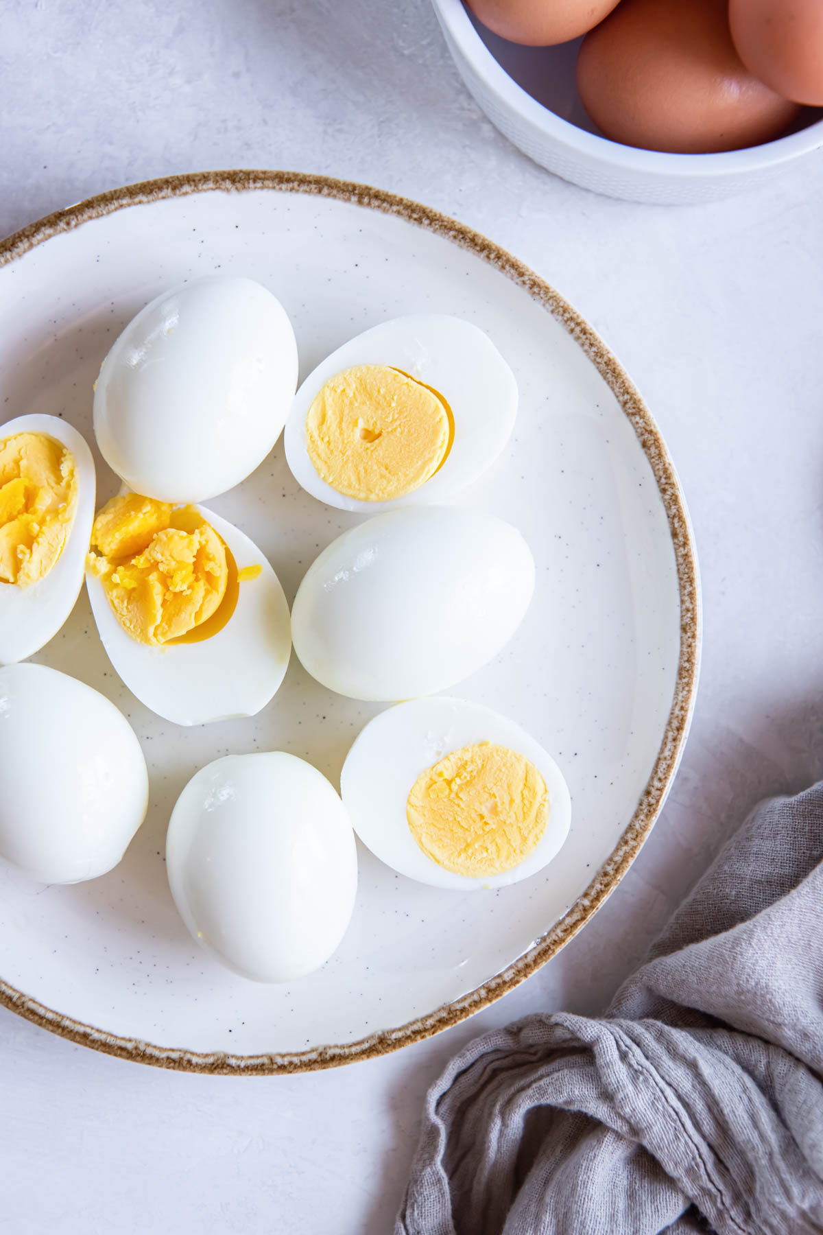 Peeled hard boiled eggs on a plate with some eggs whole and some cut in half.
