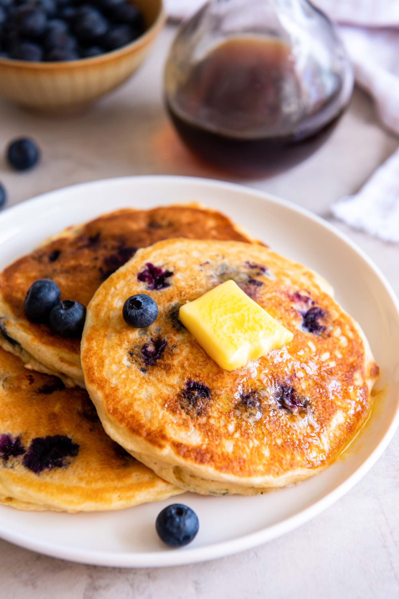 Three blueberry pancakes on a plate with a pat of butter and fresh blueberries.