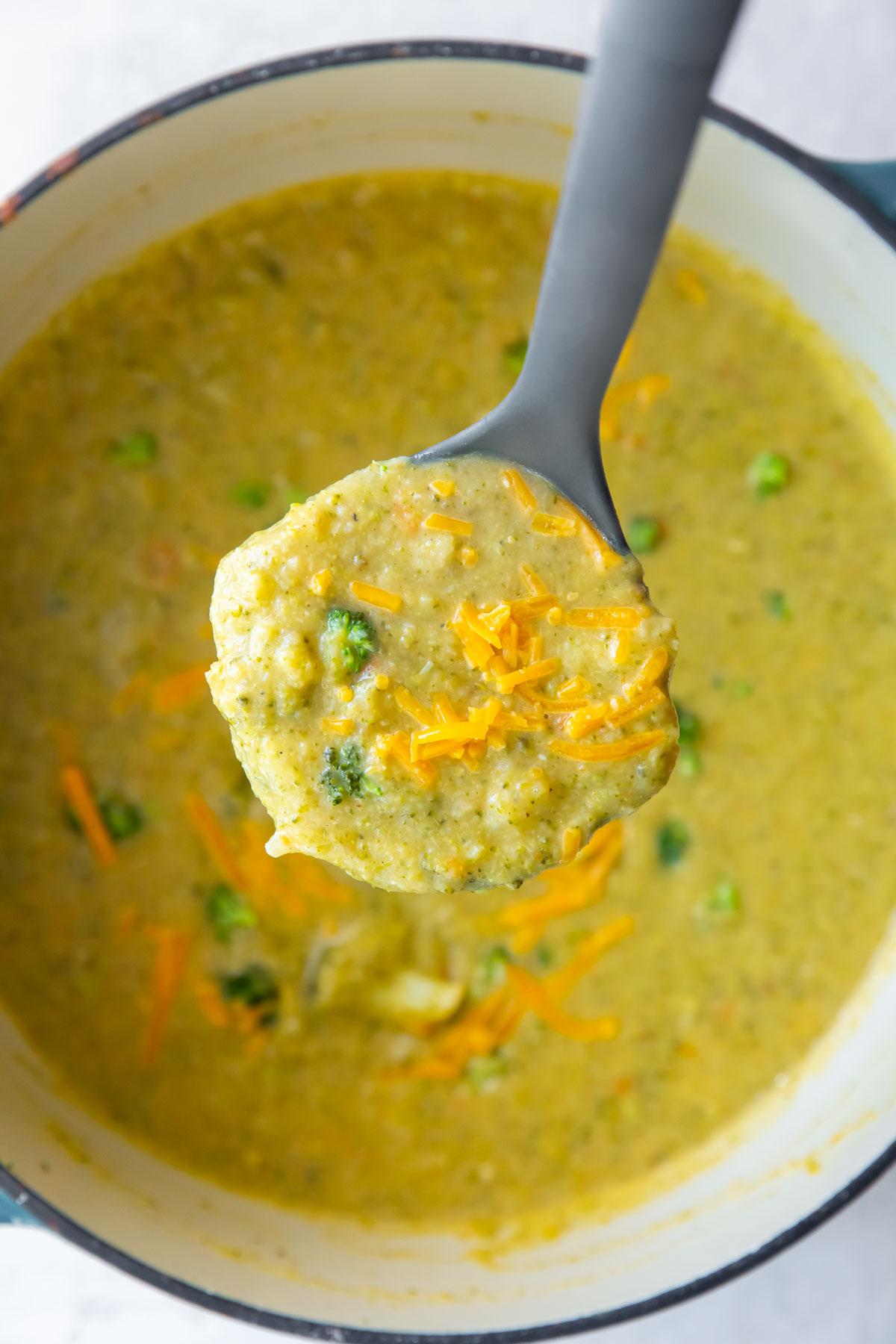 Ladle of broccoli cheddar soup held over soup pot.