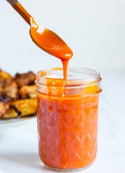 buffalo sauce dripping off of a spoon into a jar of sauce