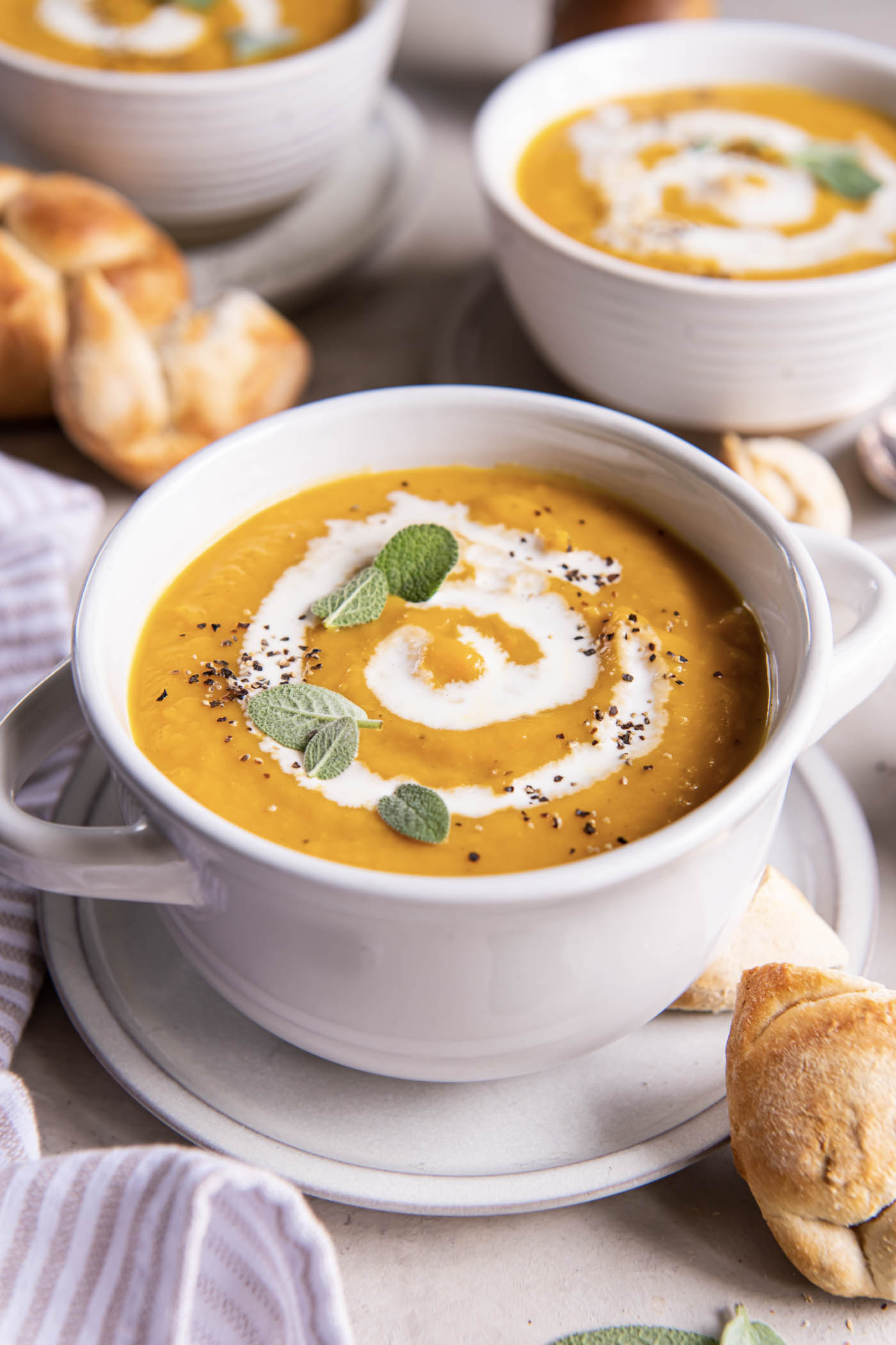 Butternut squash soup served in soup bowls with a drizzle of cream and a sprinkle of black pepper and fresh sage leaves.