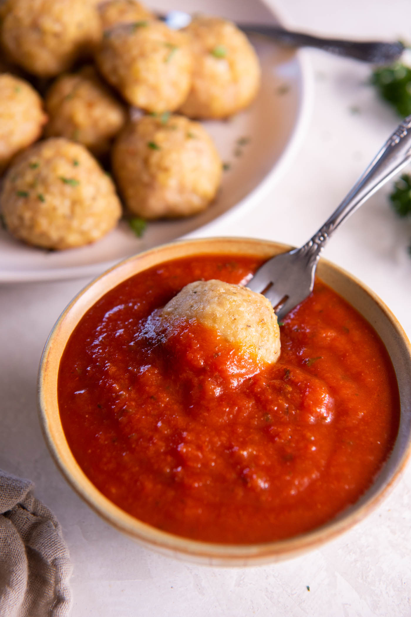 Chicken meatball on a fork dipped in small dish of marinara sauce.