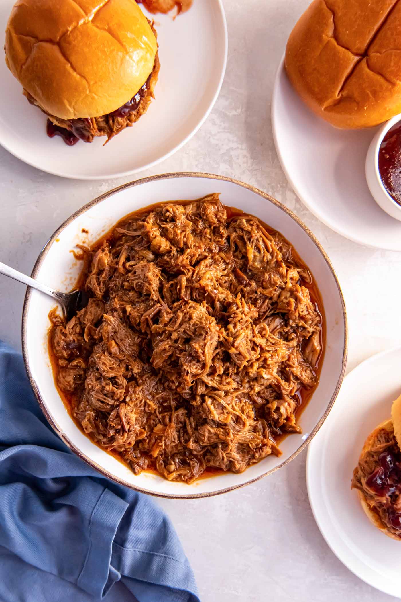 Pulled pork in a serving bowl with bbq pulled pork sandwiches served on plates.
