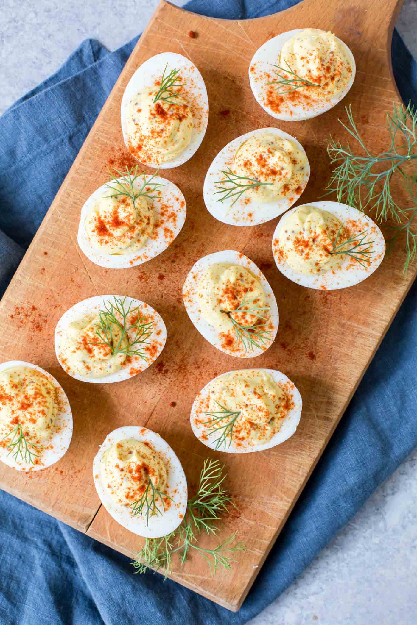 Deviled eggs with paprika and fresh dill garnish on a wood board.