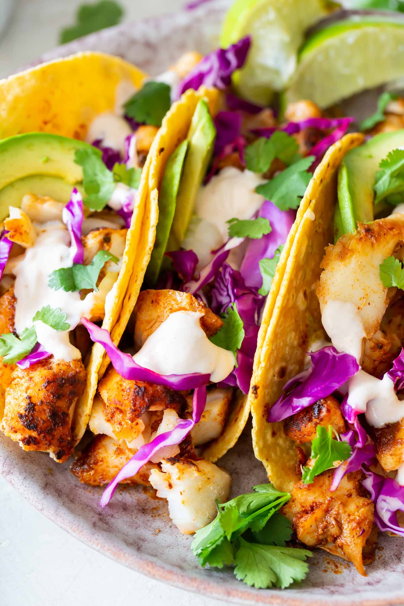 Close up of three fish tacos with cabbage, avocado and fish taco sauce.