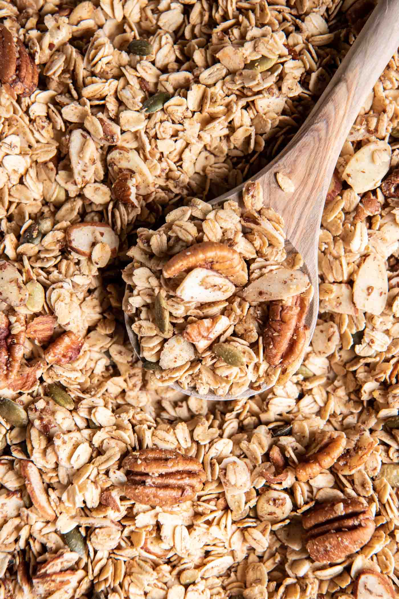 Granola on a wooden spoon set in baking sheet full of granola.