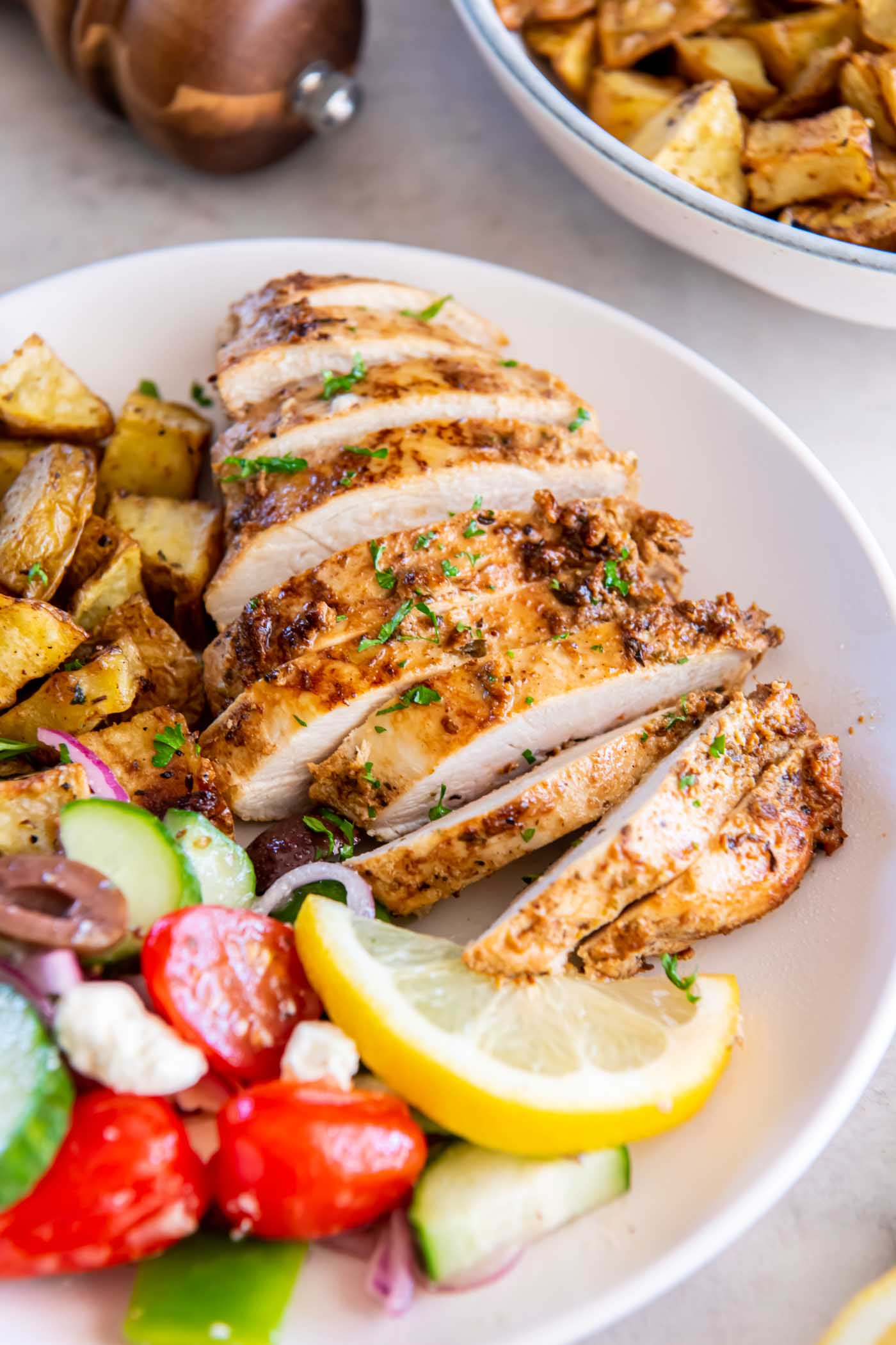 Sliced Greek chicken breast served with roasted potatoes and Greek salad.