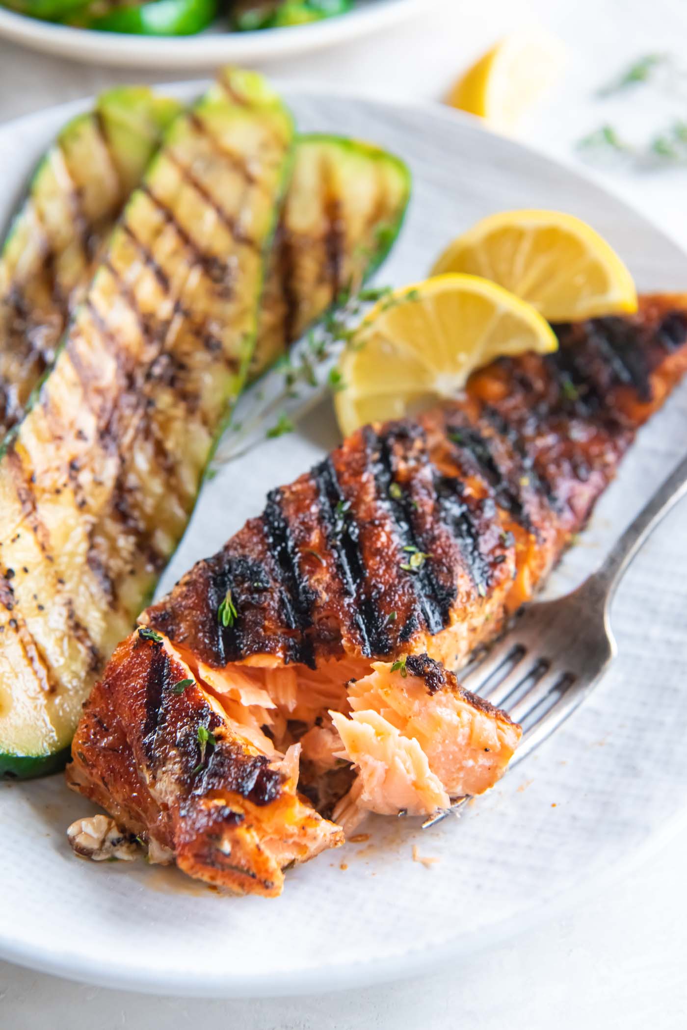 Salmon fillet partially flaked on a fork, served with grilled zucchini.