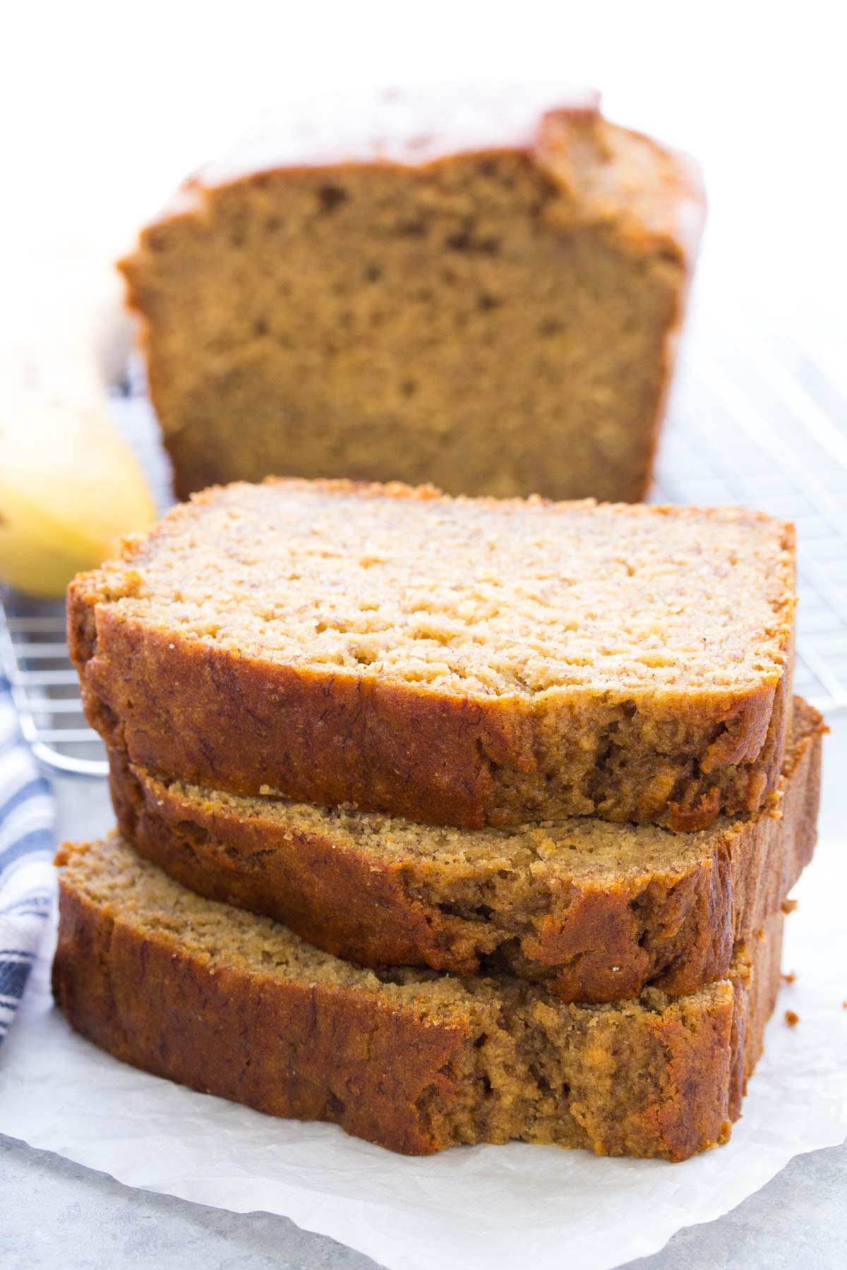 Three slices of healthy banana bread stacked with loaf in background.