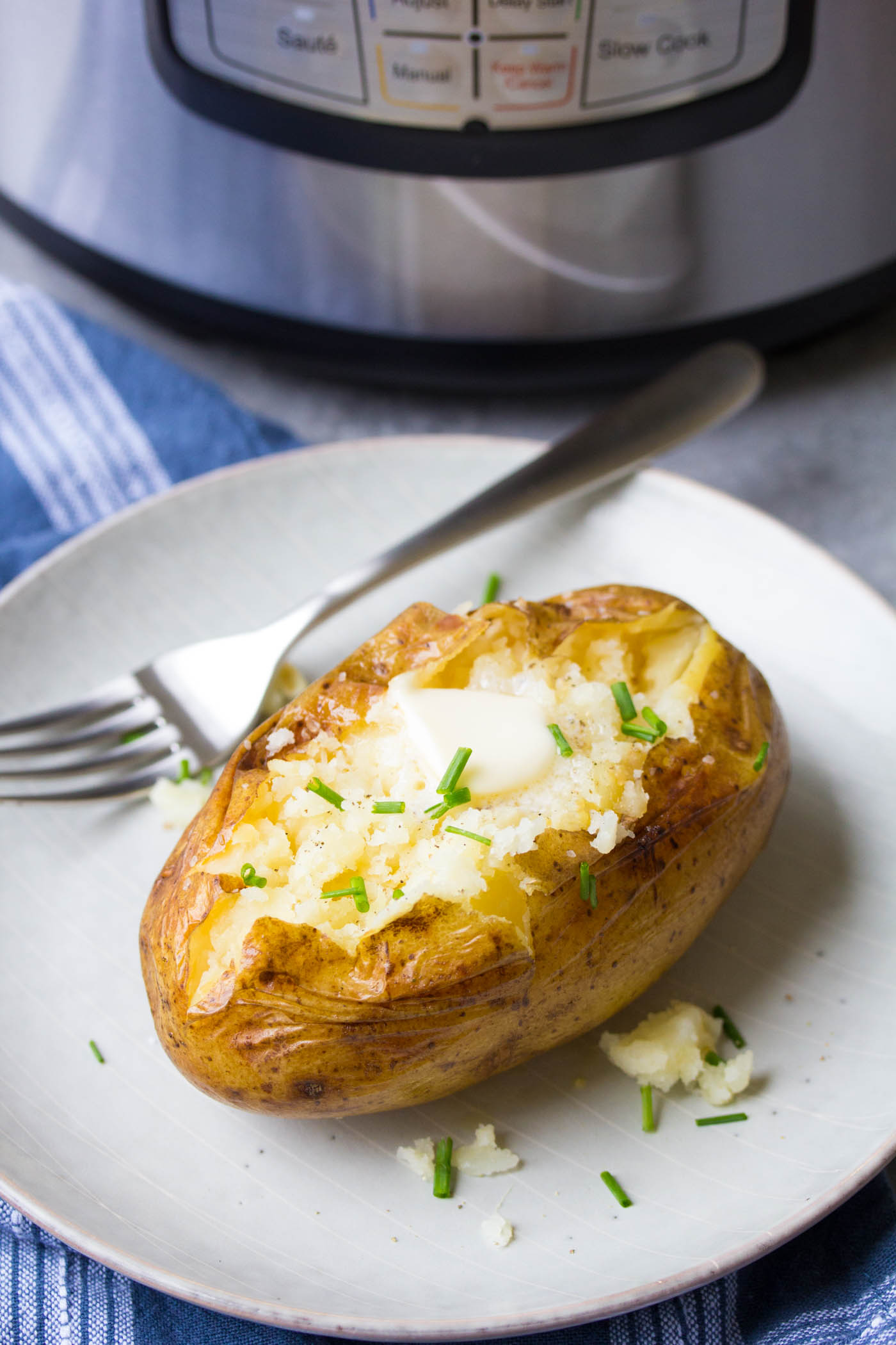 Baked potato topped with salt, pepper, butter and chives, with instant pot in the background.