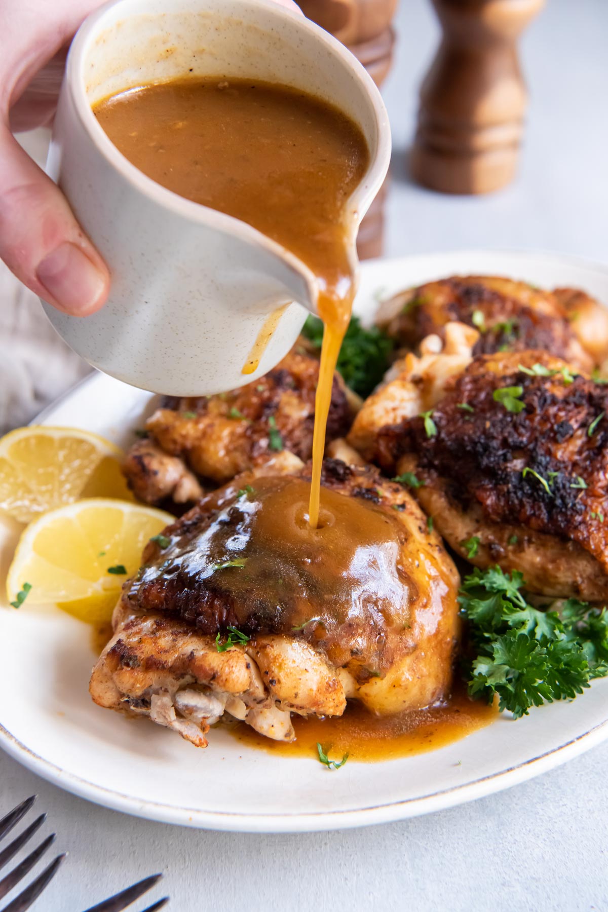 Pouring gravy onto chicken thigh on platter.