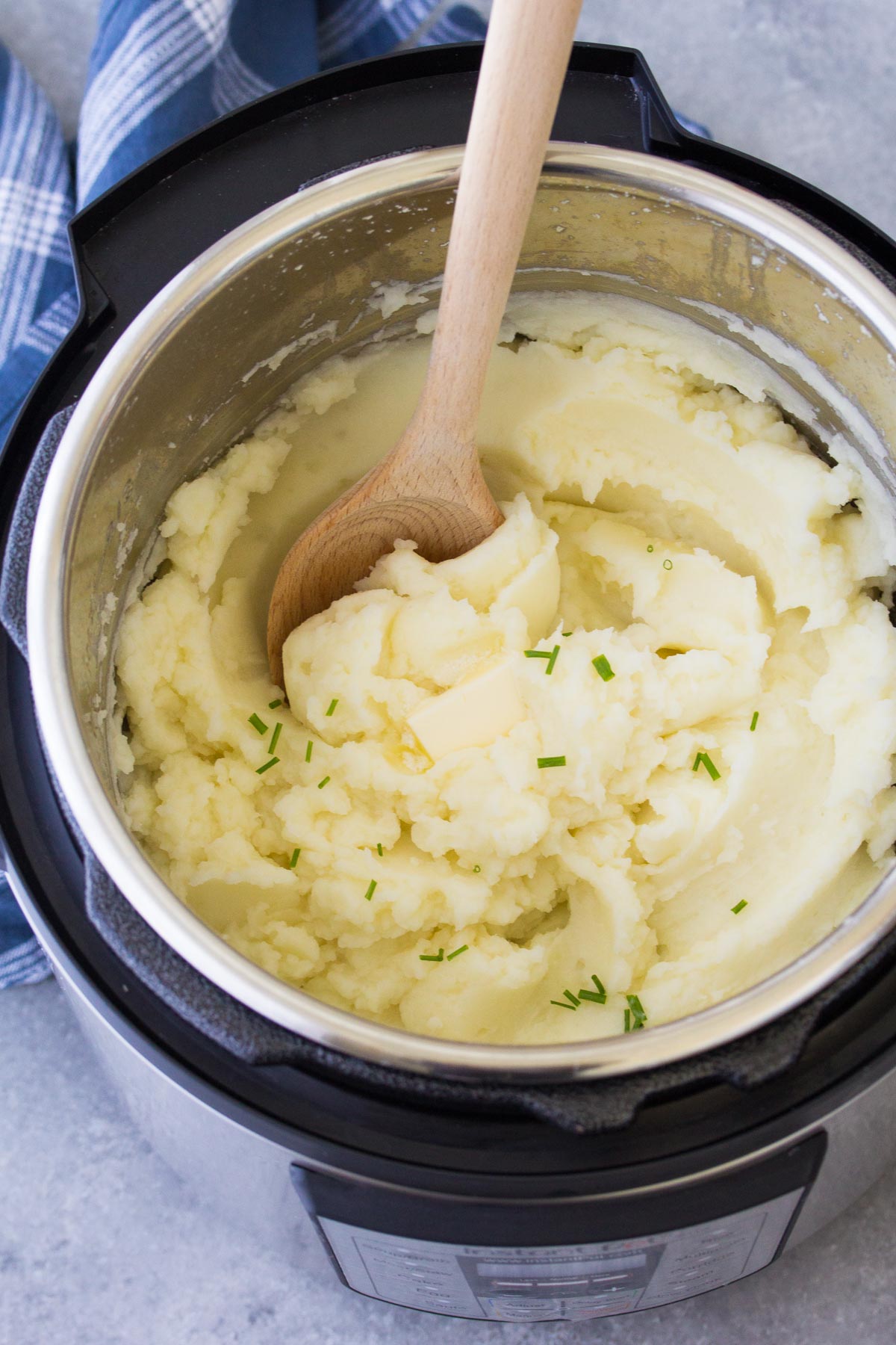 Mashed potatoes in instant pot with wood serving spoon.