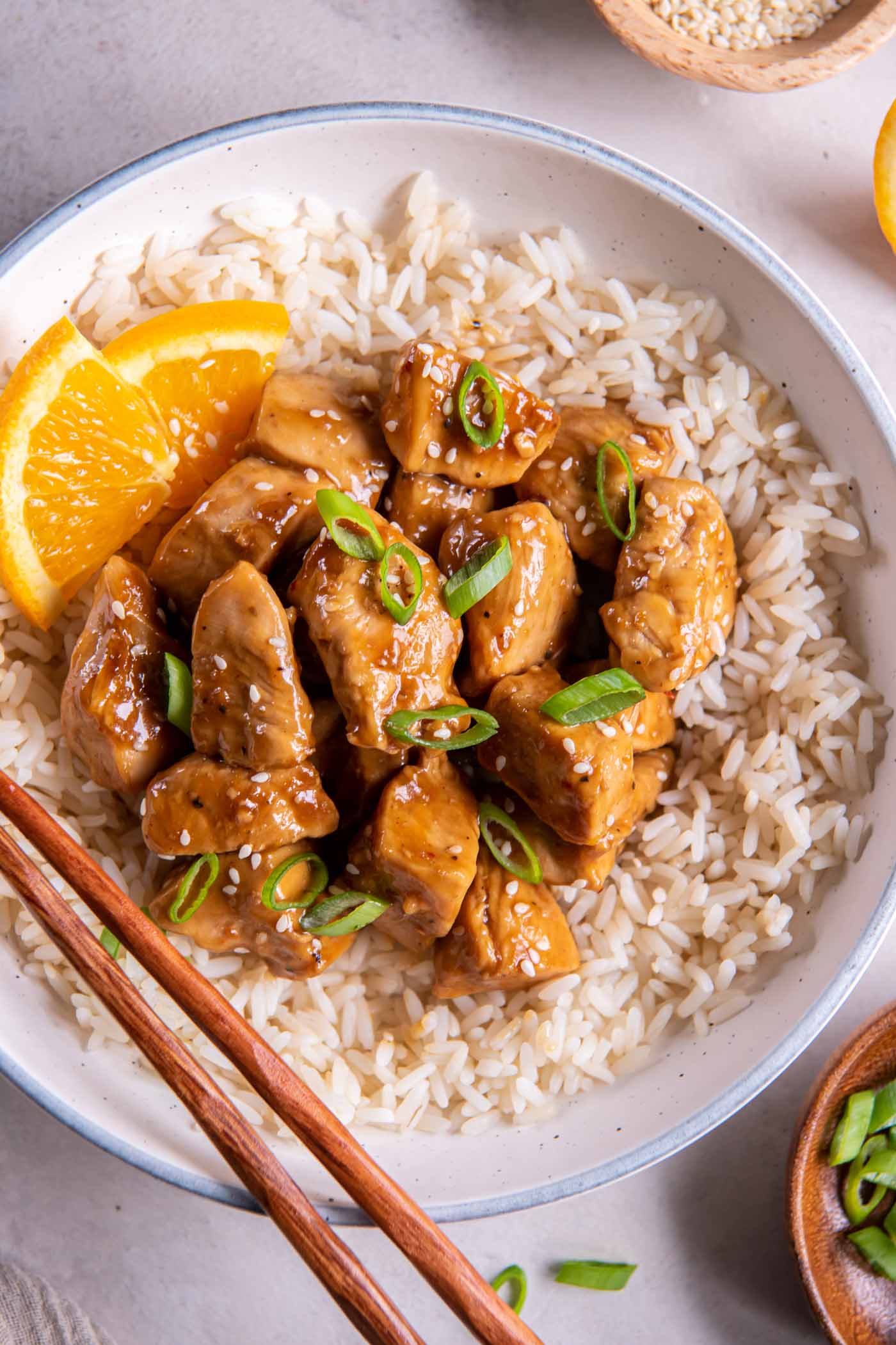 Orange chicken served over white rice and garnished with orange slices, sesame seeds and green onions.