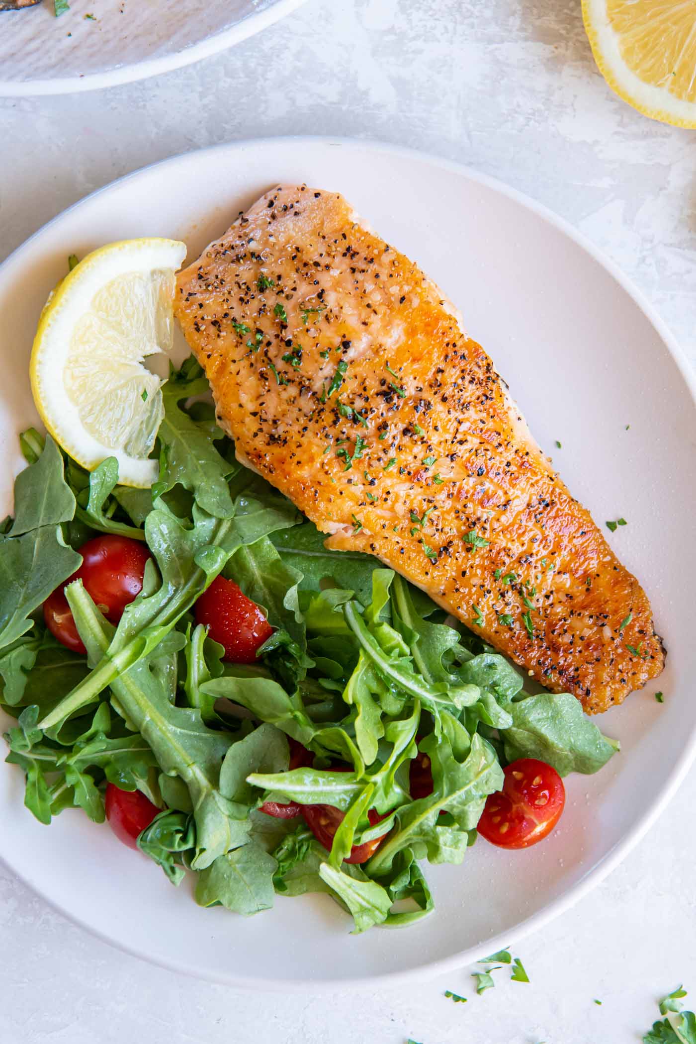 Salmon fillet served with arugula and tomato salad and a lemon wedge.