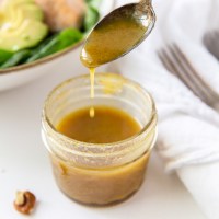 Honey mustard dressing dripping off of a spoon into a small jar of dressing.