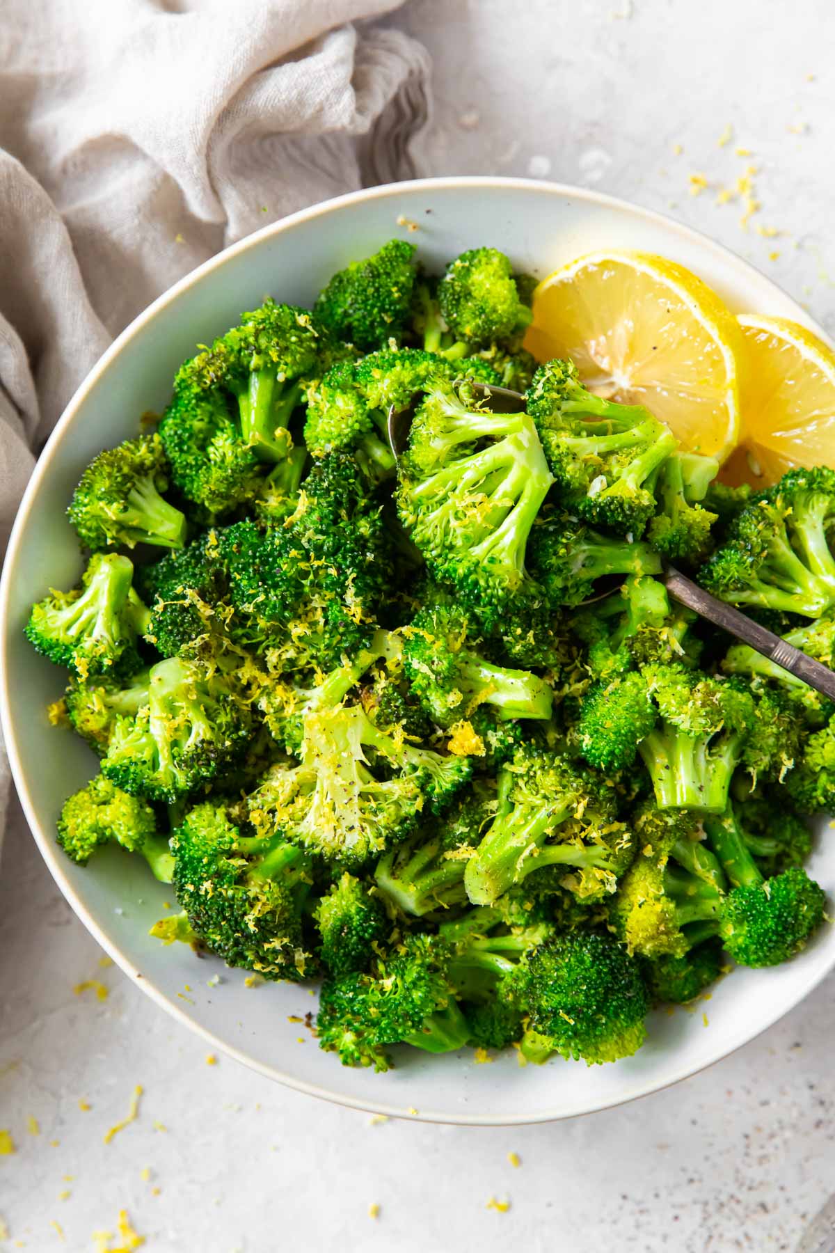 Sauteed broccoli in a serving bowl with lemon wedges.