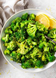 Sauteed broccoli in a serving bowl with lemon wedges.