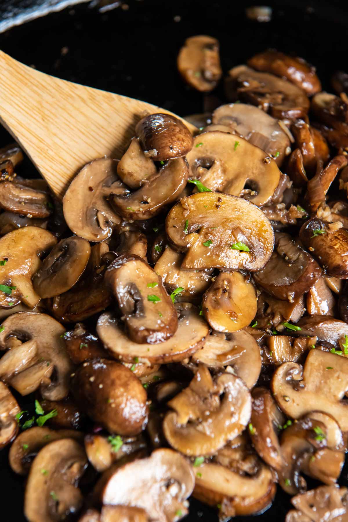 Close up of sauteed mushrooms with a wooden spoon in a skillet.