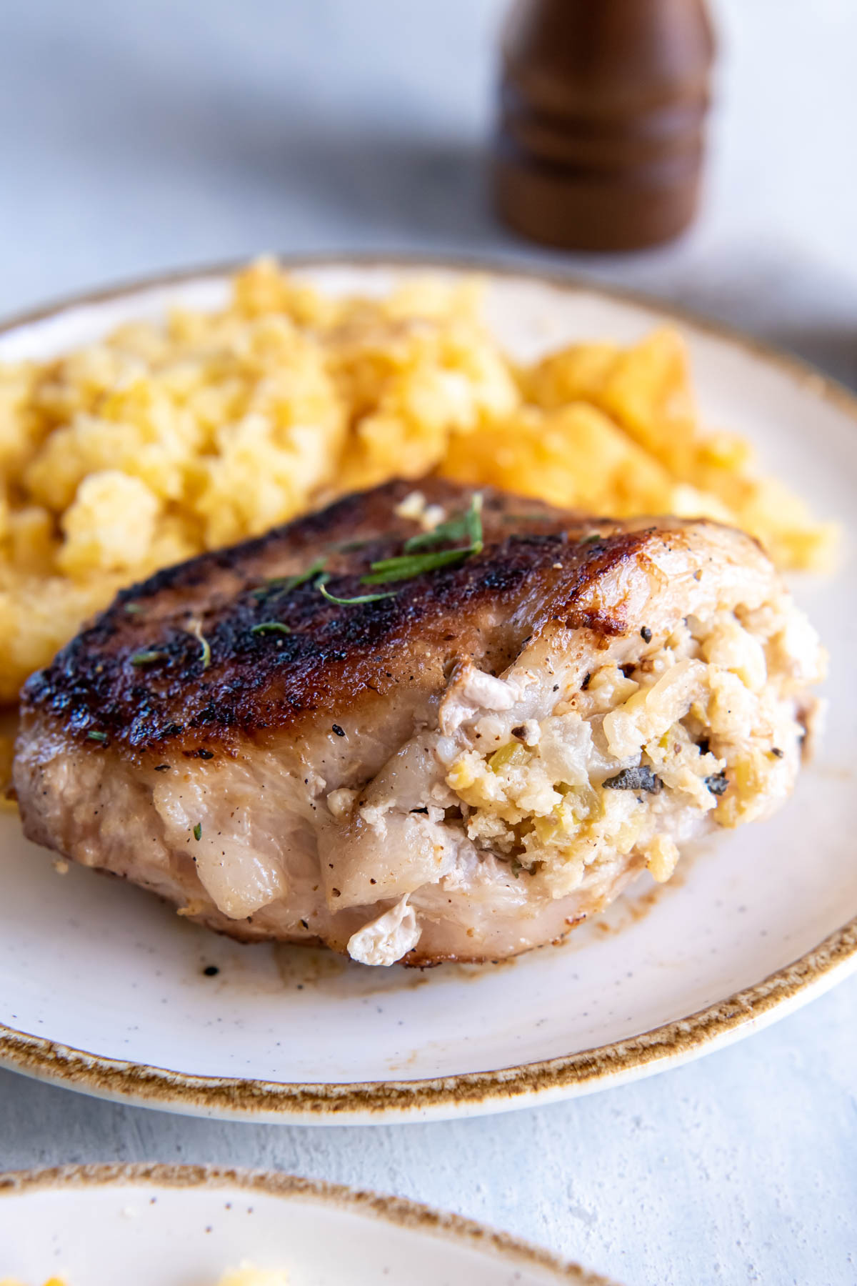 Baked pork chop stuffed with apple stuffing served on plate with corn casserole.