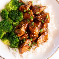 Teriyaki chicken plated with white rice, broccoli, sesame seeds and chopped green onions.