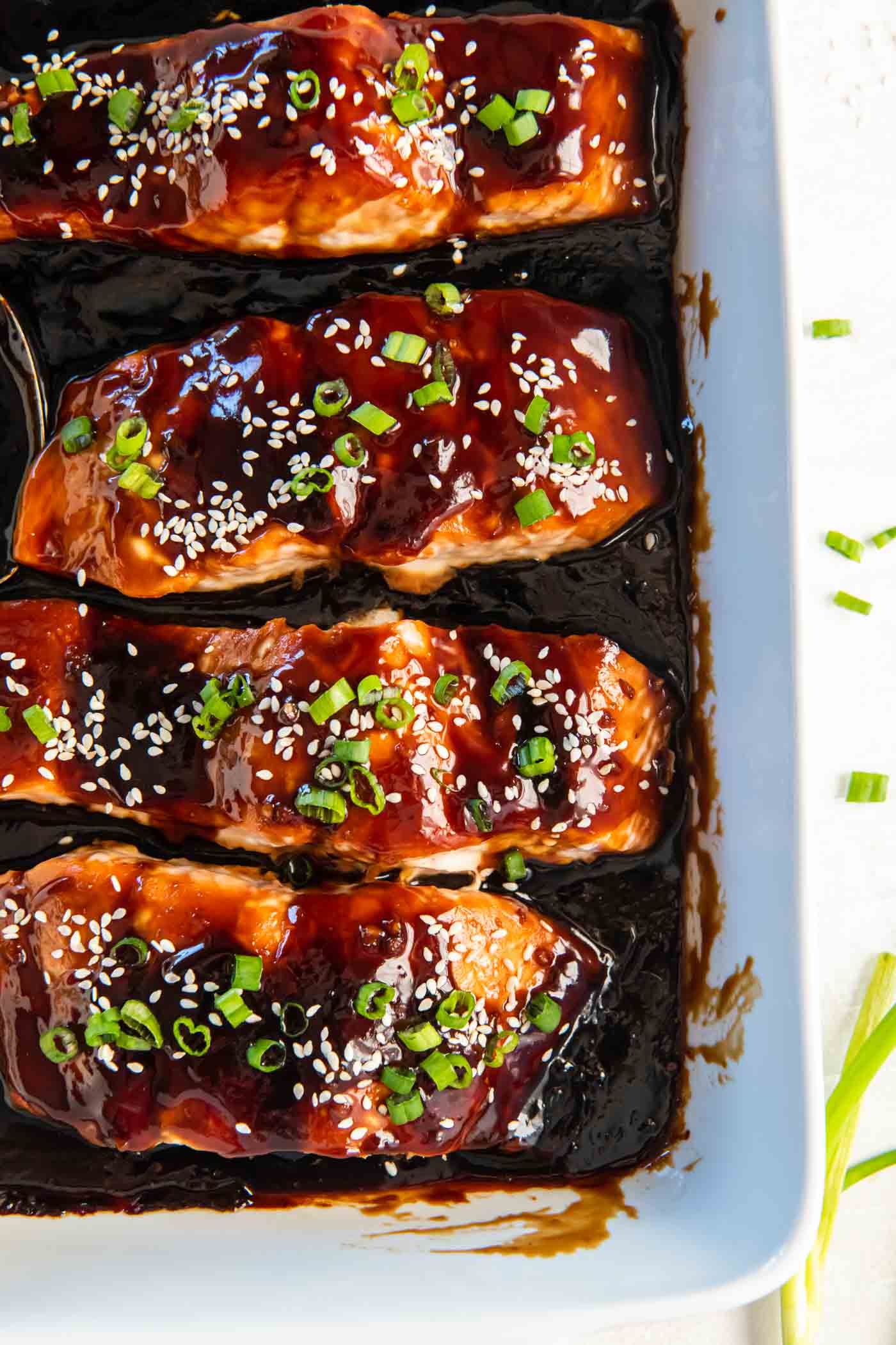 Four fillets of baked teriyaki salmon garnished with green onions and sesame seeds in a baking dish.