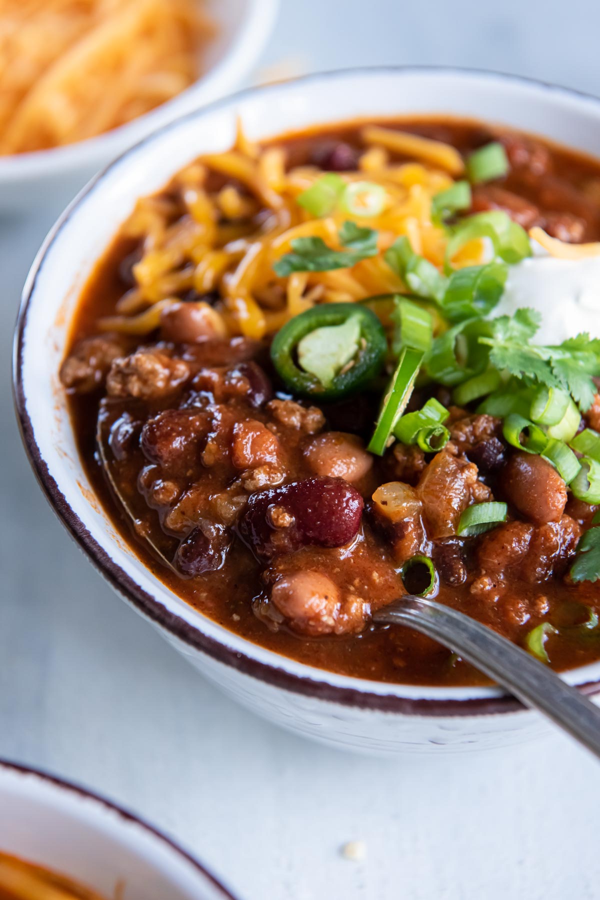 Close up of turkey chili on spoon set in bowl of chili with toppings.