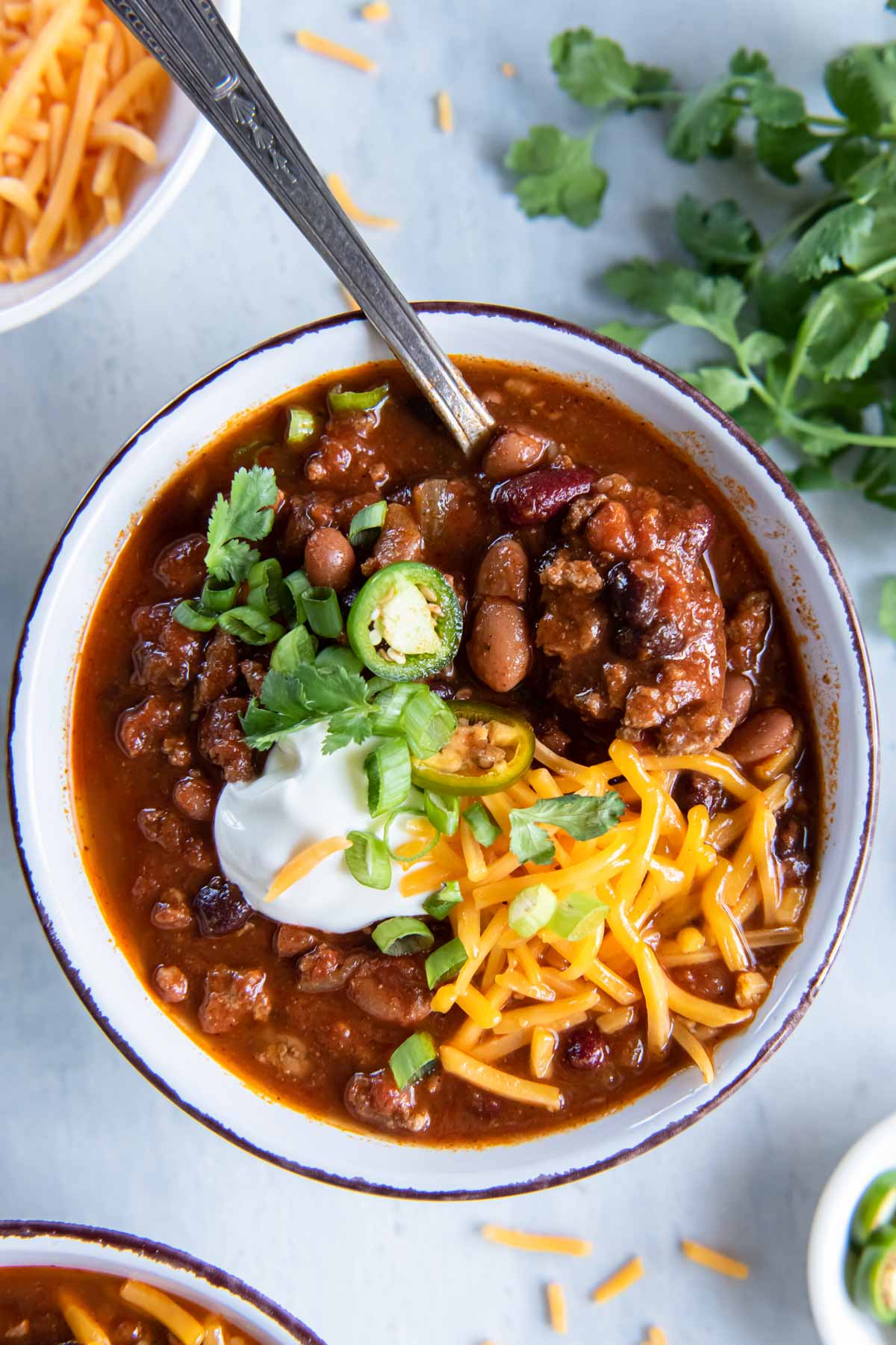 Turkey chili in a bowl with a spoon, topped with sour cream, cheddar cheese and green onions.