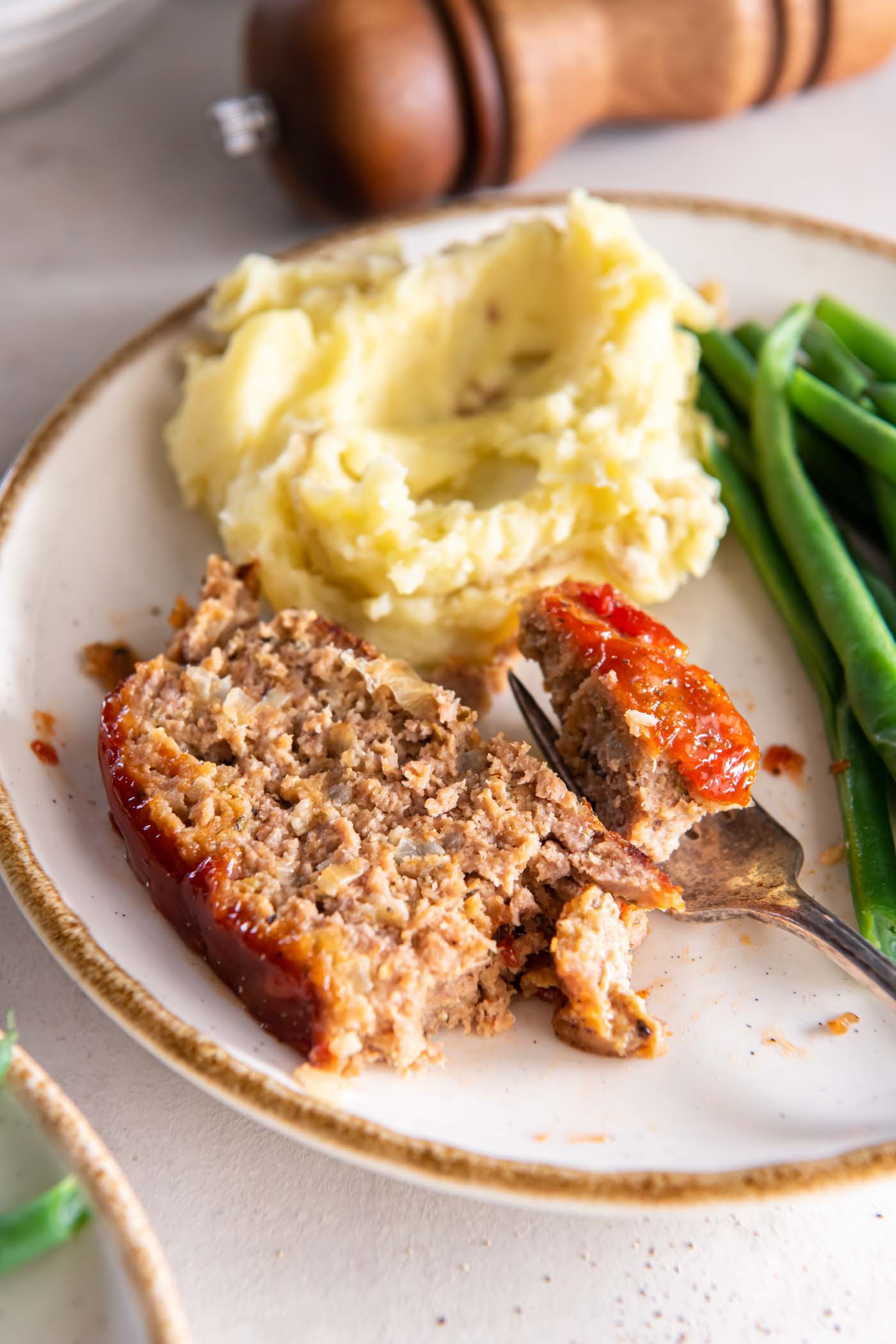 Turkey meatloaf plated with mashed potatoes and green beans with a bite of meatloaf on a fork.