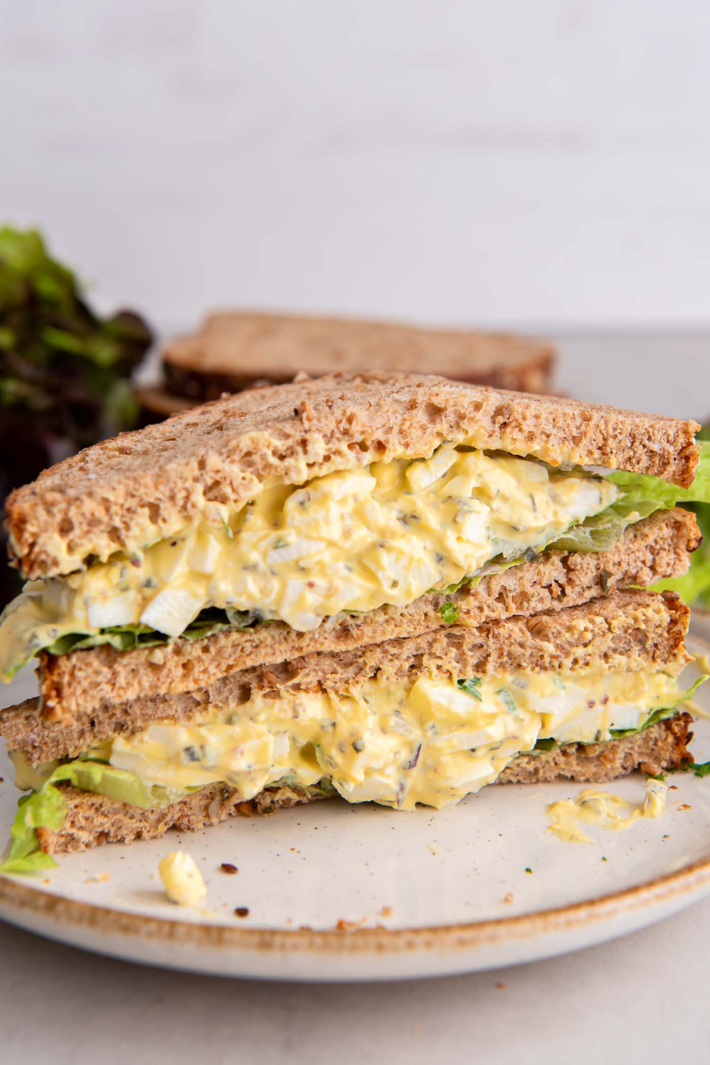 Two halves of egg salad sandwich stacked on top of each other on a plate.