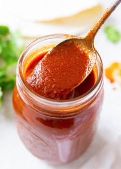Spoonful of enchilada sauce held over jar of sauce.